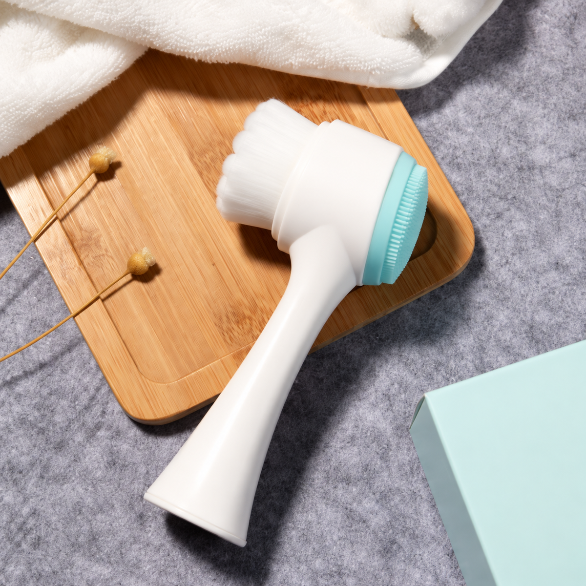 Light blue double-sided facial cleansing brush with white handle and bristles